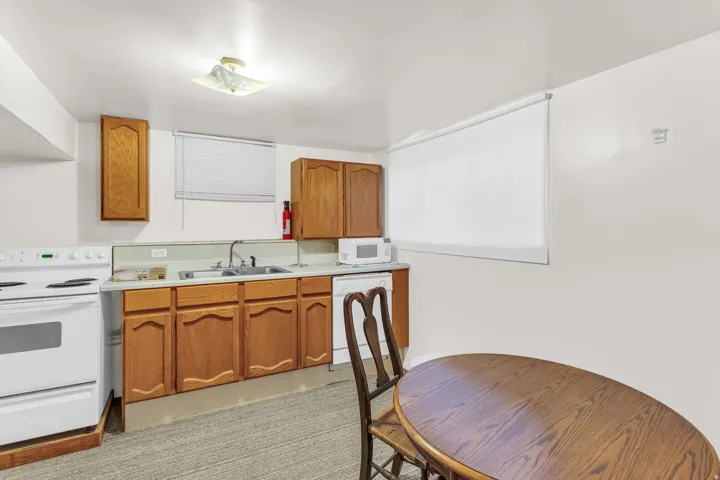 Kitchenette featuring wood-finish cabinetry, a stainless steel sink, and white appliances including a range and dishwasher