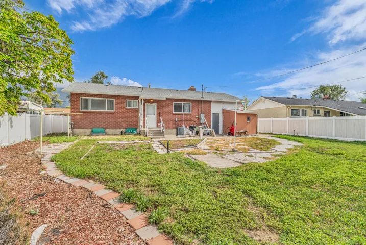 Expansive backyard featuring a red brick exterior, white vinyl fencing, a detached storage shed, and a concrete patio