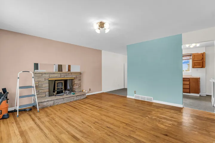 Stone-clad fireplace with wood-burning insert, wood flooring, and recessed lighting