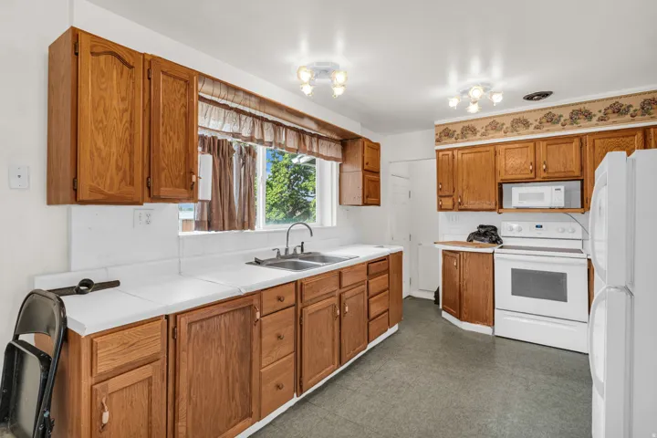 Kitchen featuring wood-finish cabinetry, a double basin sink, and a white appliance suite