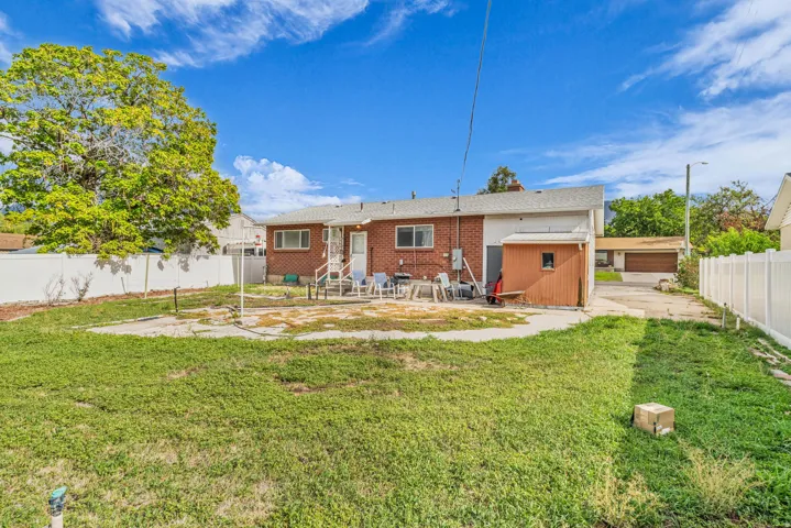 Expansive backyard with a large grass area, white privacy fencing, a red brick exterior, a back entry door, and a detached storage shed