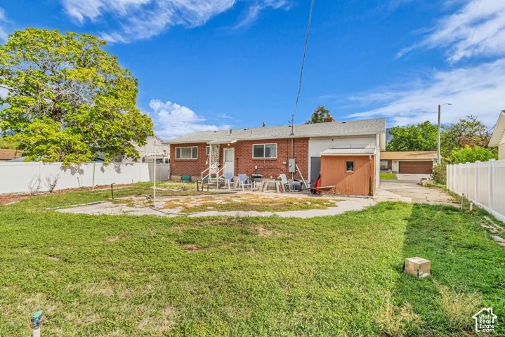 Expansive backyard with a large grass area, white privacy fencing, a red brick exterior, a back entry door, and a detached storage shed