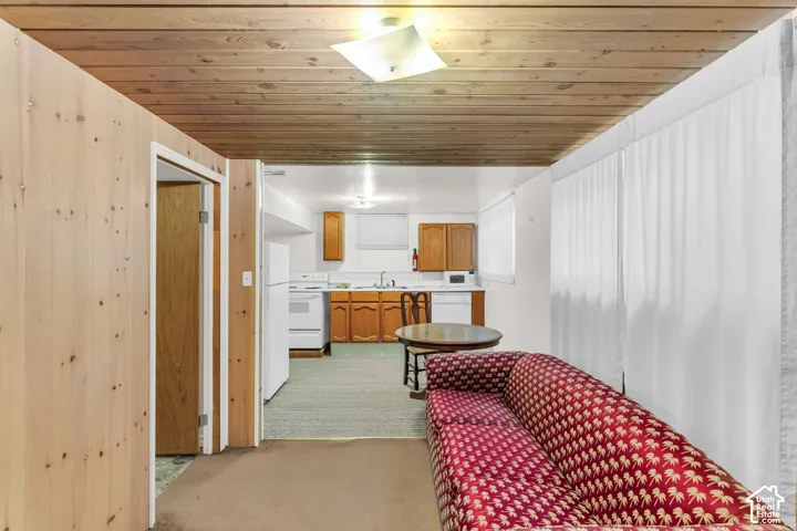 Wood-paneled ceiling, white upper cabinetry, wood-finish lower cabinetry, built-in sink, and white appliances