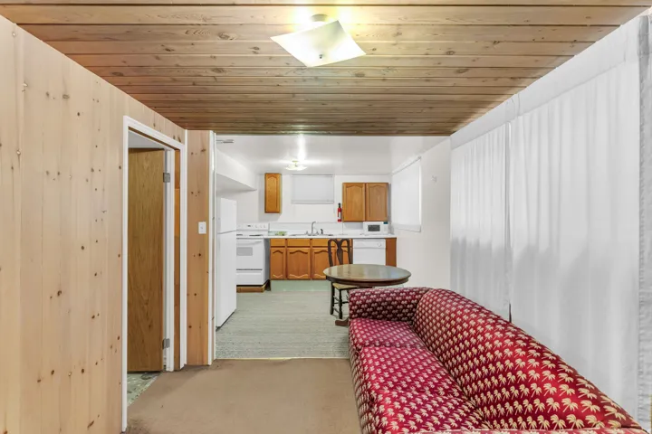 Wood-paneled ceiling, white upper cabinetry, wood-finish lower cabinetry, built-in sink, and white appliances