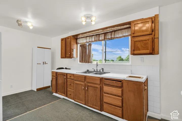 Kitchen with wood cabinetry, white countertops, tile backsplash, and a double basin sink