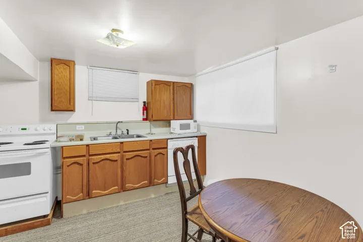 Kitchenette featuring wood-finish cabinetry, a stainless steel sink, and white appliances including a range and dishwasher