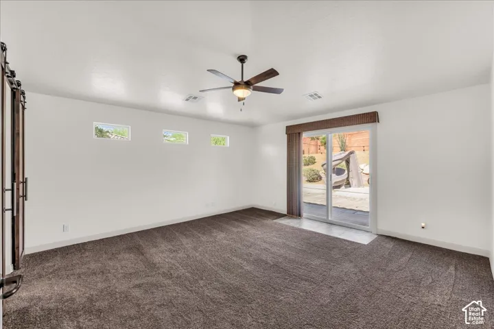 Sliding glass door, neutral carpeting, ceiling fan, three transom windows, barn door with dark hardware