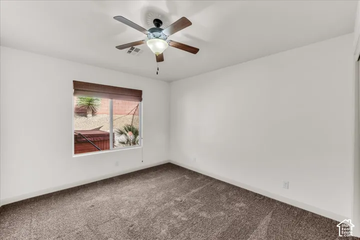 Neutral wall paint, ceiling fan, window with woven shade, and carpet flooring
