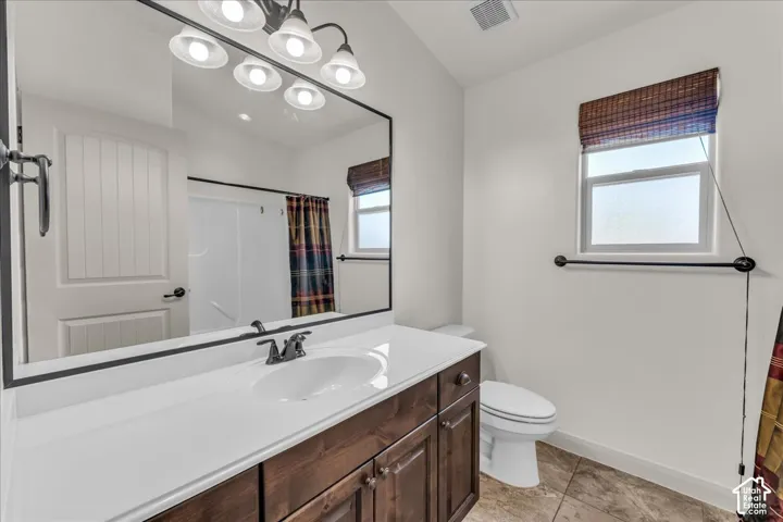 Bathroom featuring a wood-finish vanity with an integrated sink, a large rectangular mirror, and a window with a woven shade