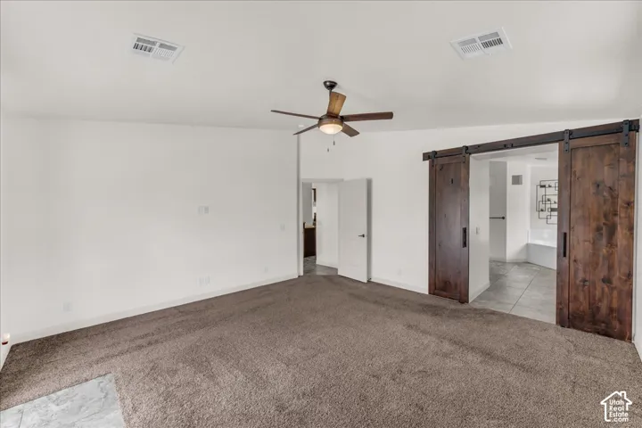 Spacious room with carpet flooring, a ceiling fan, and rustic wood-finish barn doors