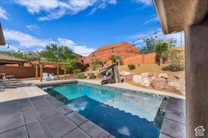 Backyard featuring a built-in swimming pool, integrated water slide, a wooden pergola, string lighting, and a terraced landscape with natural rock elements