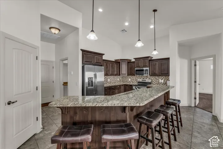 Kitchen featuring dark wood cabinetry, stainless steel appliances, a tiled backsplash, and a breakfast bar with stone-finish countertops