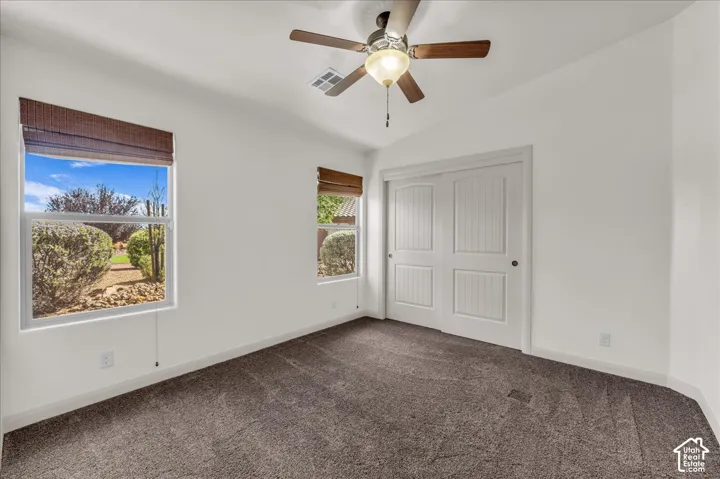 Vaulted ceiling featuring a ceiling fan, dual windows with woven wood shades, and a dual-door closet