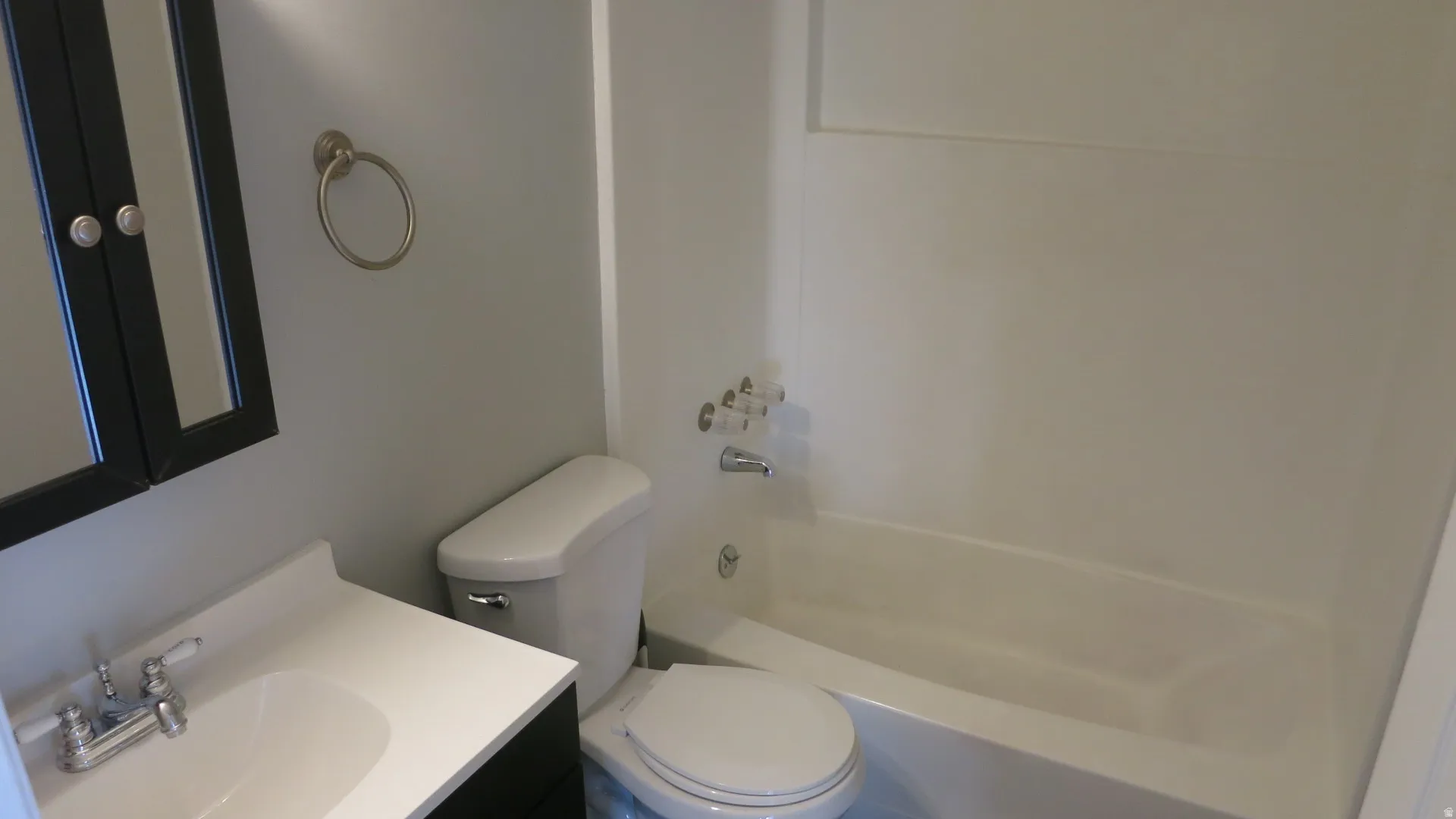 Integrated bathtub and shower combination with white surround, white toilet, vanity with integrated white sink, chrome faucet, and dark wood-finish medicine cabinet