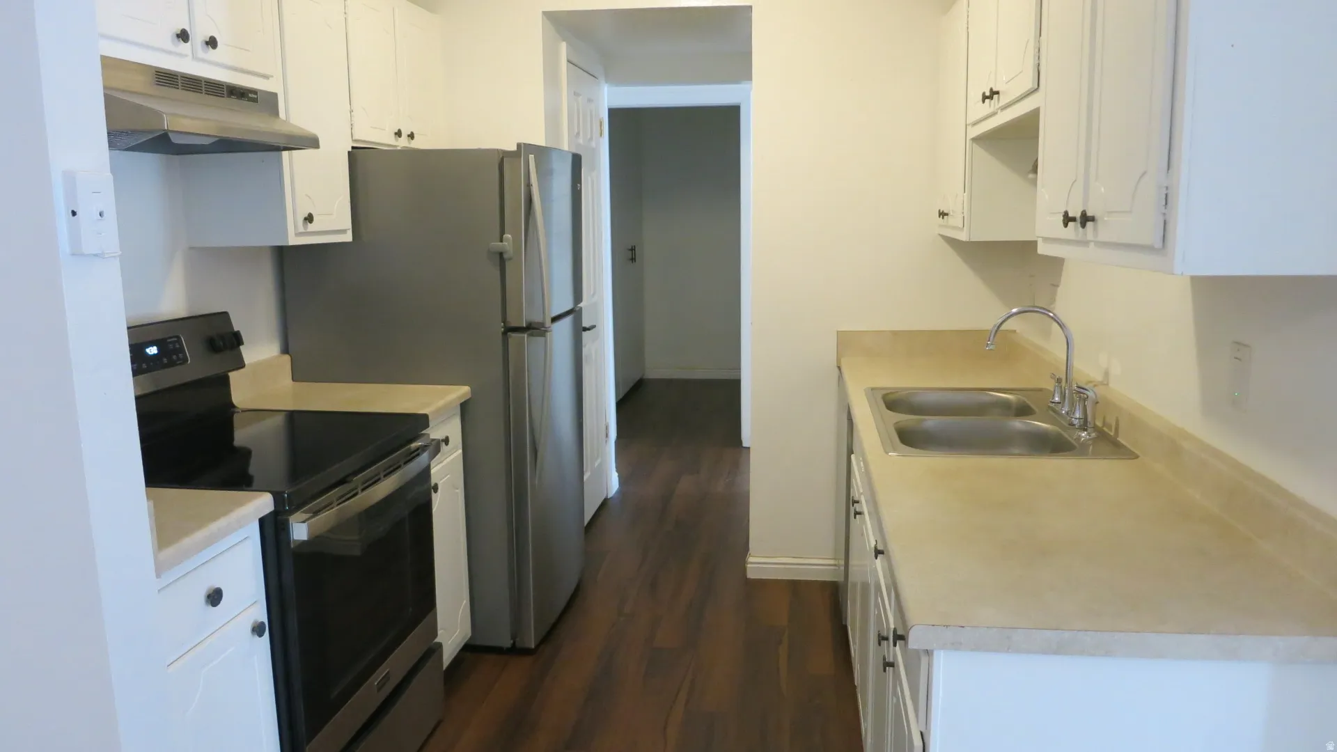 Kitchen featuring wood-finish flooring, white cabinetry with dark hardware, a stainless steel electric range, a stainless steel refrigerator, and a double basin sink