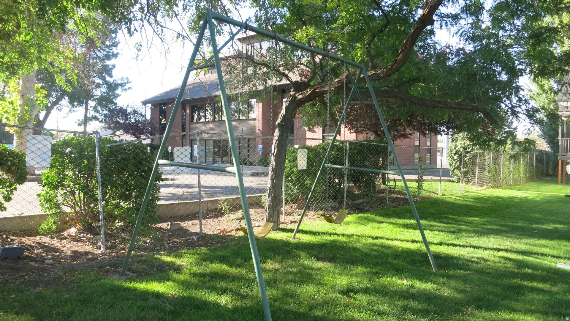 Expansive green lawn with swing set, mature trees and a chain-link fence