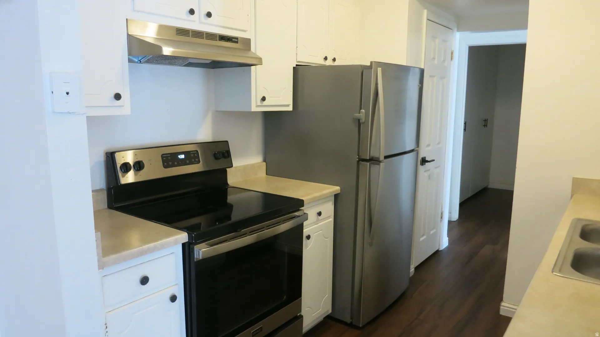 Kitchen featuring stainless steel appliances, white cabinetry, dark wood-finish flooring, and a double basin sink