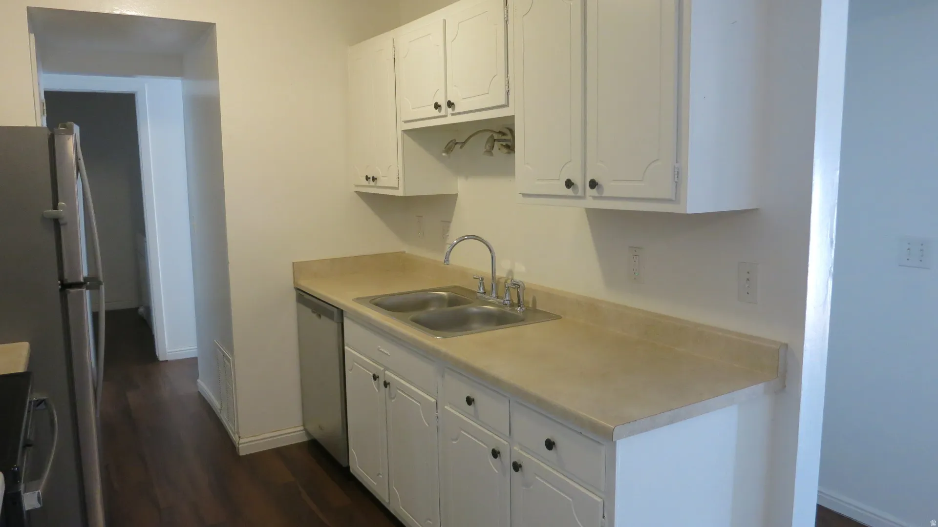 Kitchen featuring white cabinetry, a double basin stainless steel sink, light-toned countertop, and wood-finish flooring