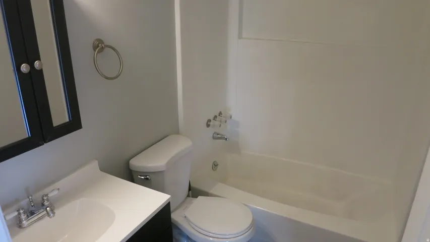 Integrated bathtub and shower combination with white surround, white toilet, vanity with integrated white sink, chrome faucet, and dark wood-finish medicine cabinet