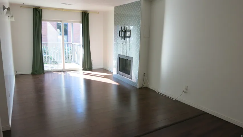 Wood-finish flooring, tiled fireplace surround, integrated fireplace, and sliding glass door to a balcony with white railings