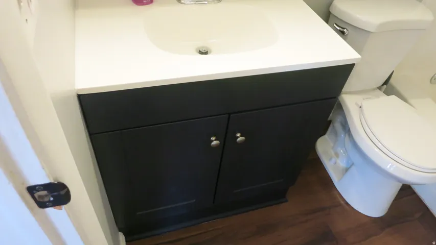 Brand New Vanity with dark cabinetry and integrated white sink, complemented by white toilet and wood-finish flooring