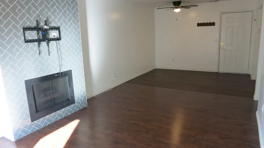 Wood-finish flooring, white walls, decorative fireplace surround, and a ceiling fan with integrated lighting