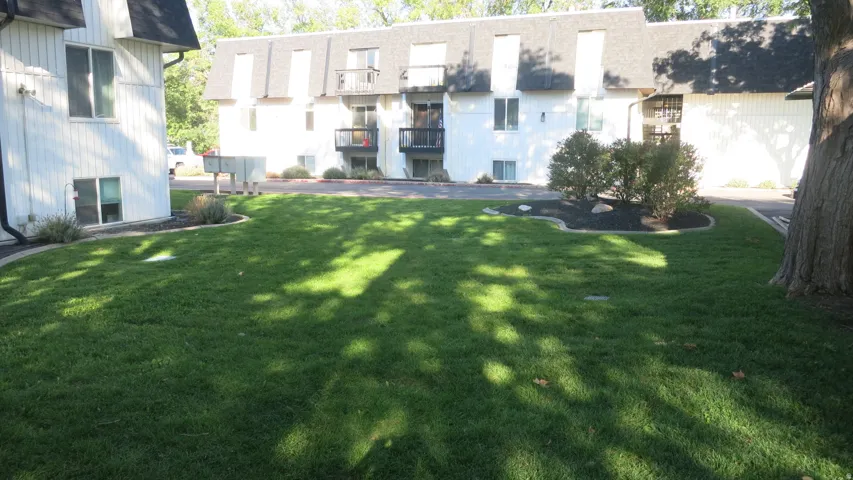 Manicured lawn, mature trees, landscaped beds, and white siding