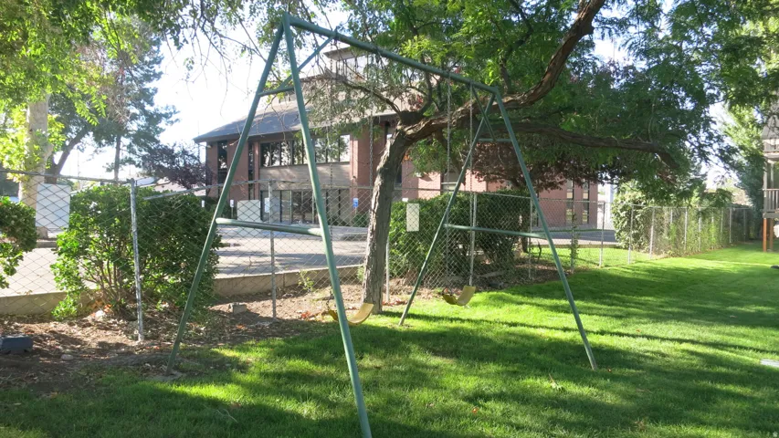 Expansive green lawn with swing set, mature trees and a chain-link fence