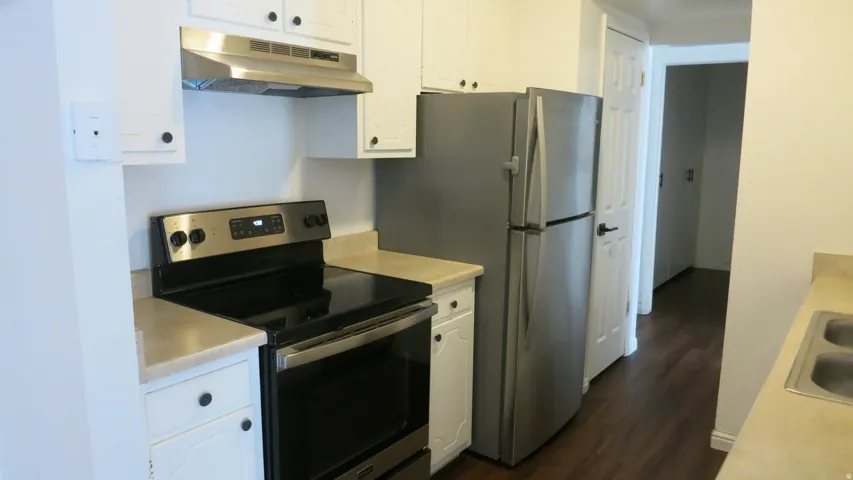 Kitchen featuring stainless steel appliances, white cabinetry, dark wood-finish flooring, and a double basin sink