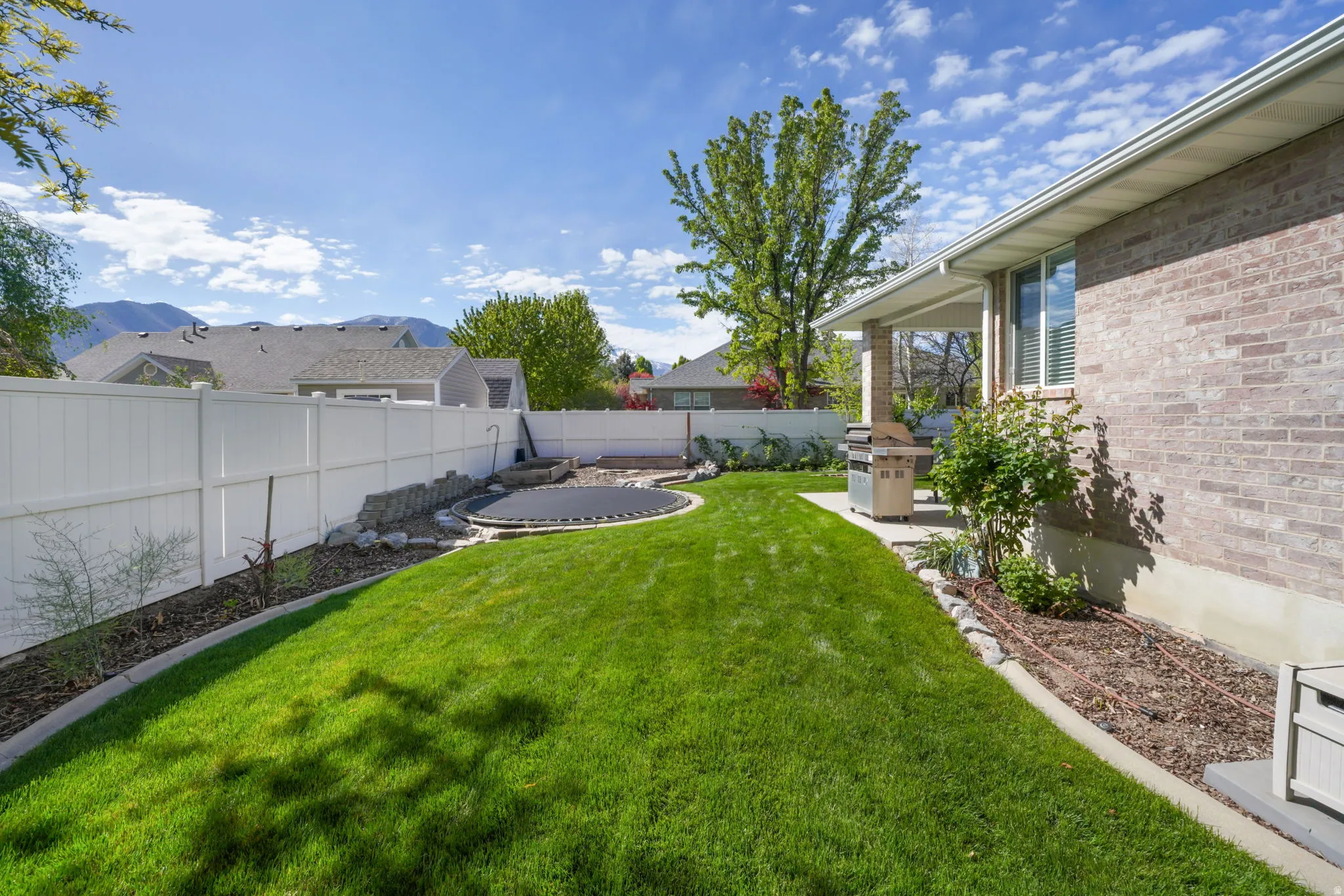 Manicured lawn, full privacy fencing, brick exterior, covered patio, and established landscaping