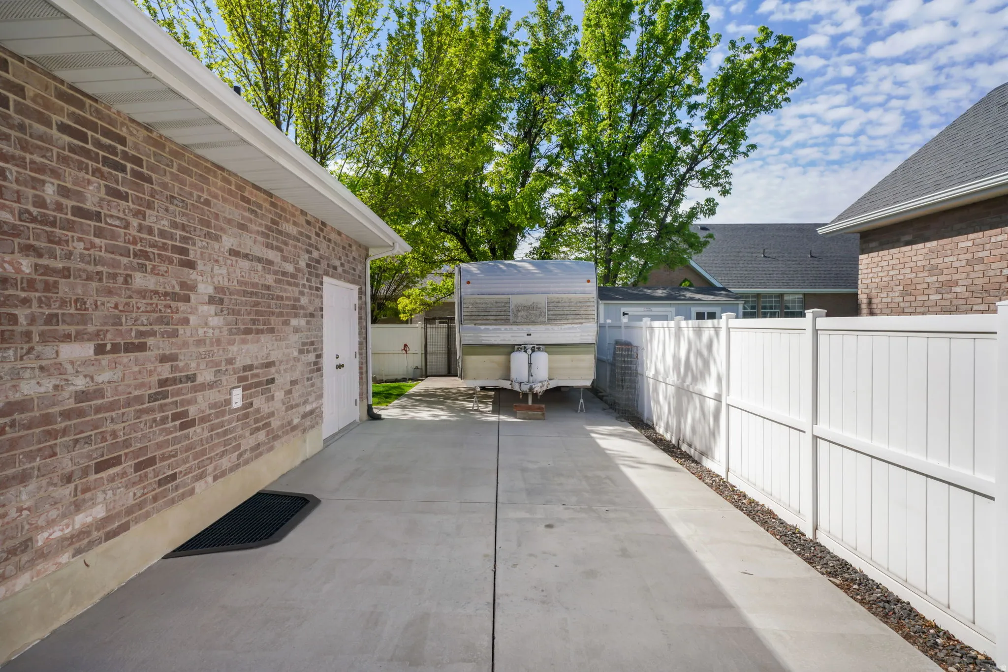 Brick exterior with a white service door, concrete driveway, and white privacy fencing
