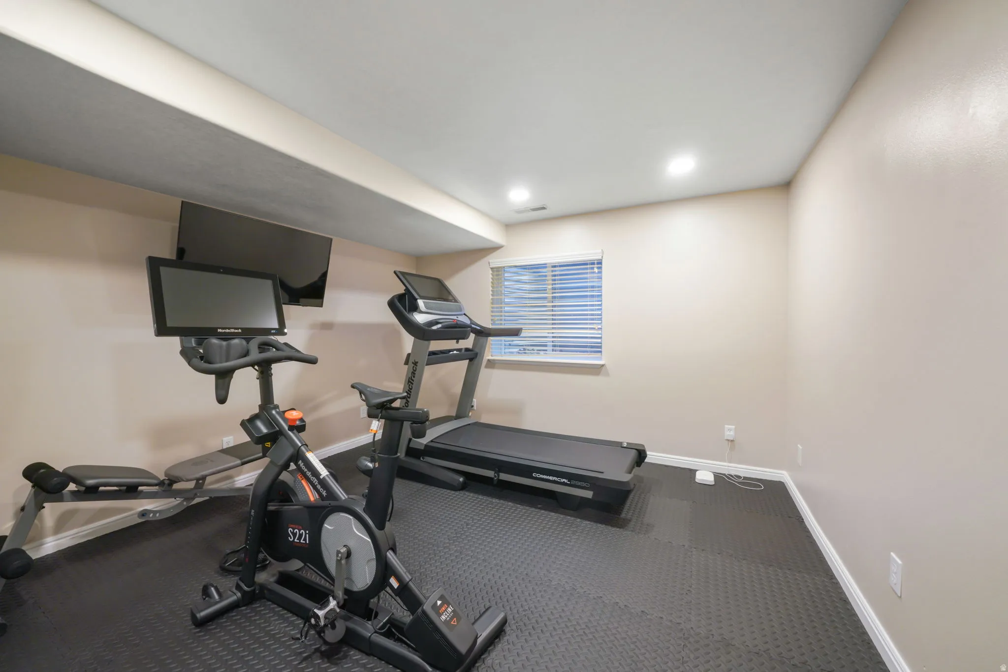 Recessed lighting, window with horizontal blinds, wall-mounted television, and padded flooring