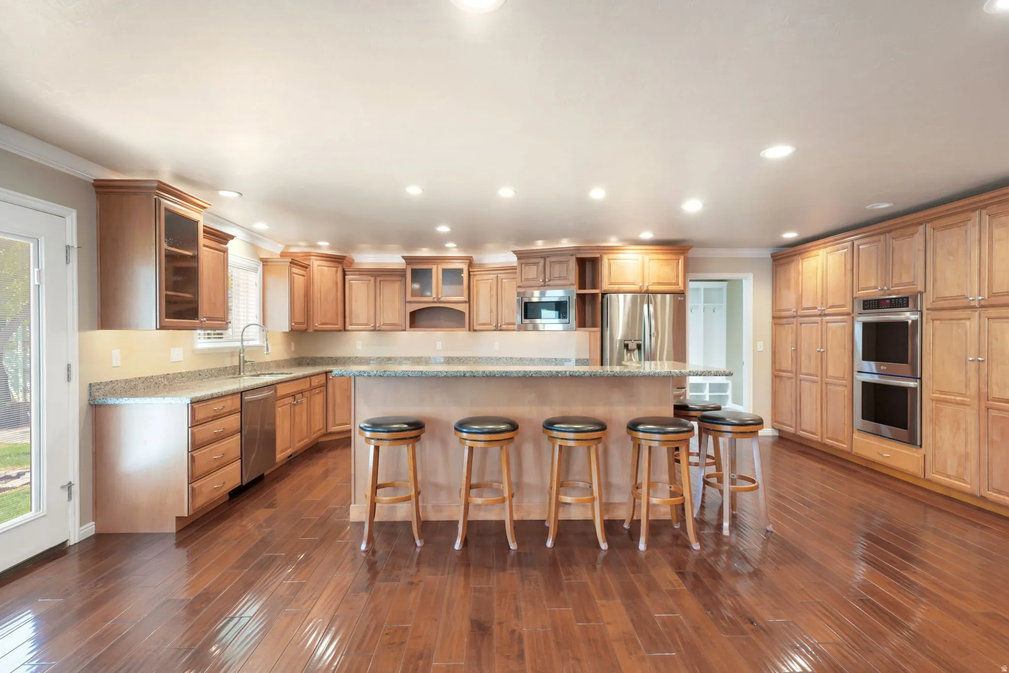 Expansive kitchen featuring wood-finish flooring, abundant cabinetry, stainless steel appliances, recessed lighting, and a center island with bar seating