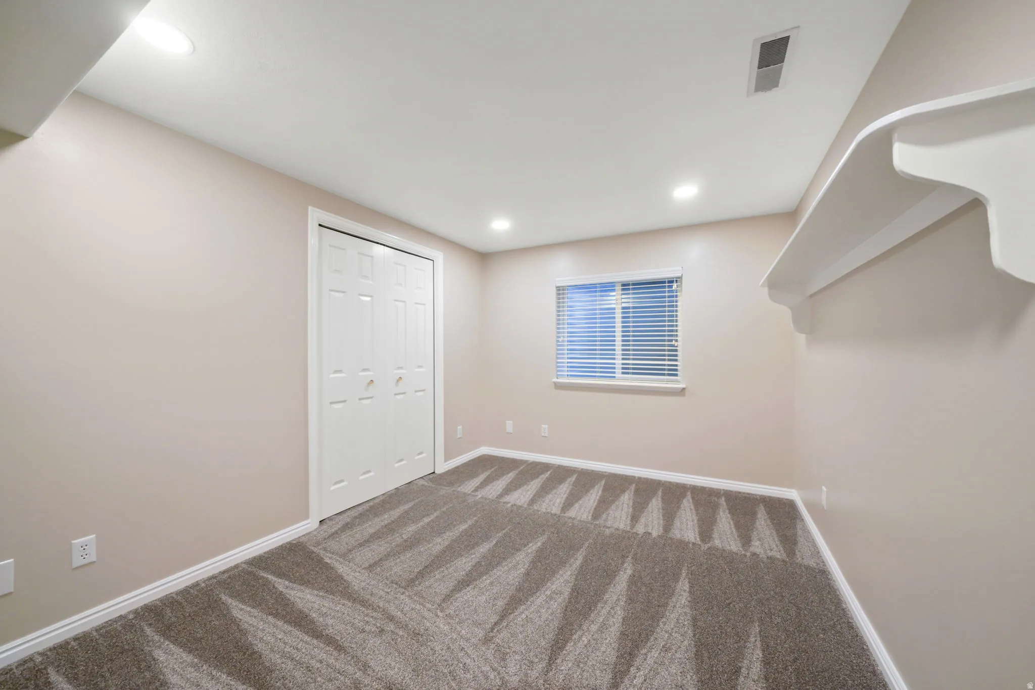 Recessed lighting, patterned carpet, window with blinds, white trim, and a built-in decorative shelf