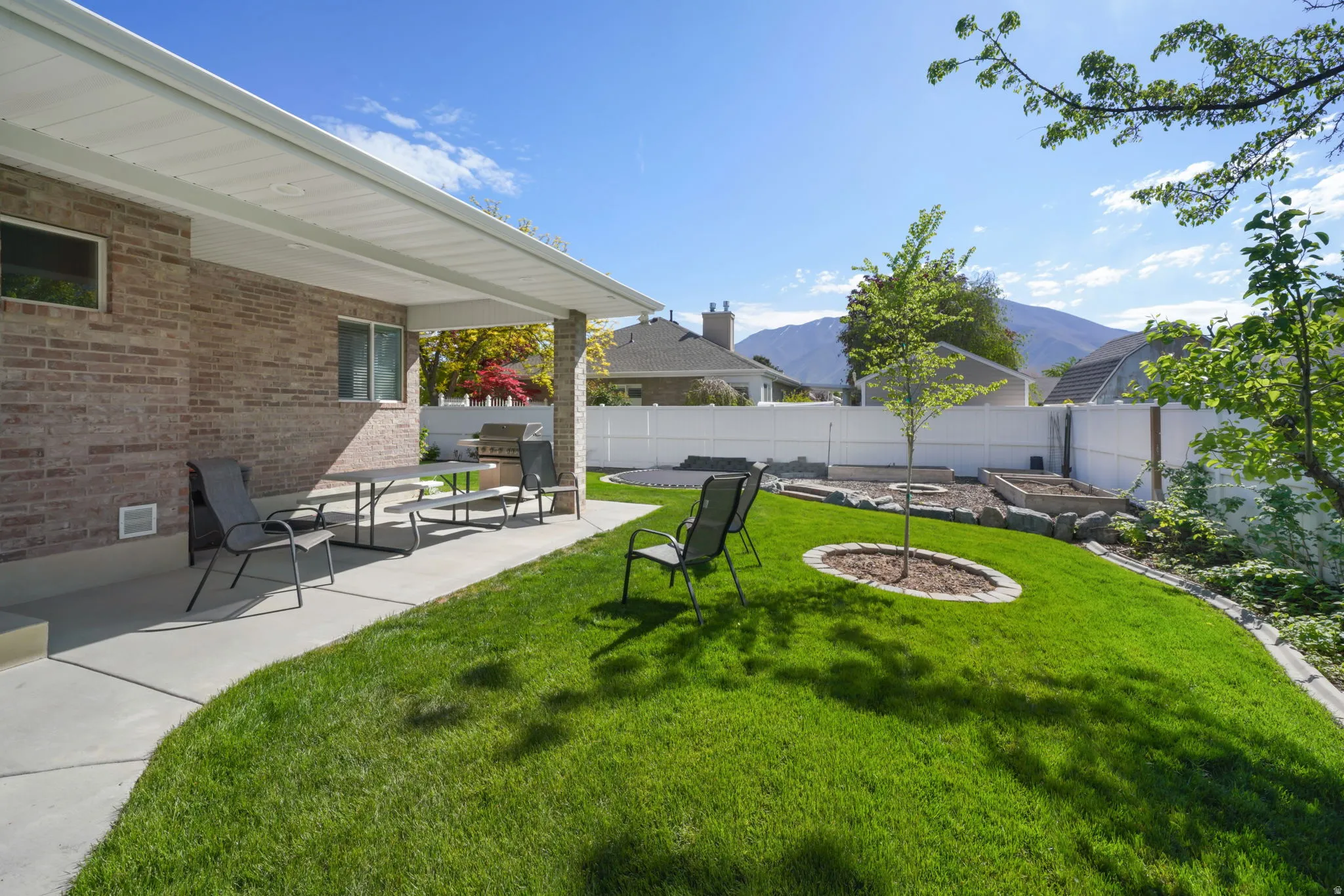 Brick exterior featuring a covered patio, expansive lawn, white privacy fencing, and raised garden beds