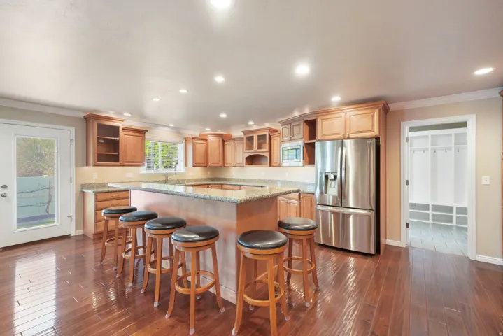 Expansive kitchen featuring wood-finish flooring, light wood cabinetry, a large kitchen island with a stone countertop, stainless steel appliances, and recessed lighting