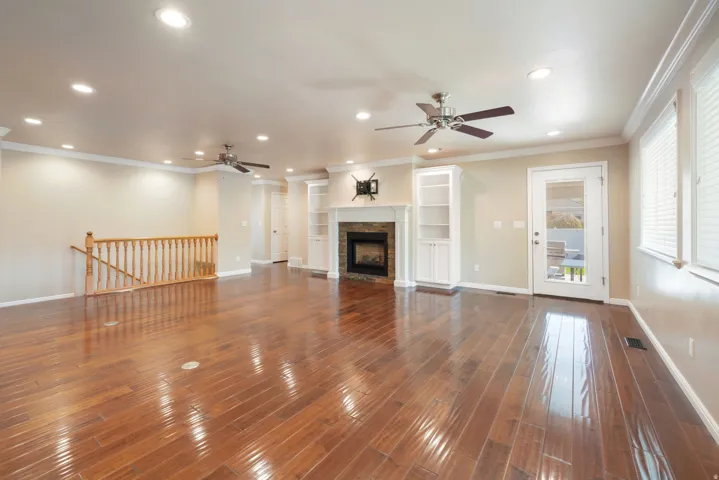 Hardwood-finish flooring throughout, recessed ceiling lighting, stone-surround fireplace with built-in shelving, two ceiling fans, and multiple windows