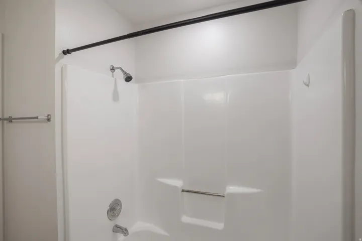White shower-over-tub unit with integrated shelf and grab bar