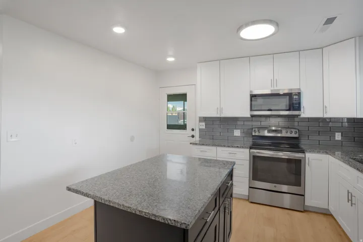 Kitchen featuring a central island with a stone-finish countertop, white cabinetry with stainless steel hardware, stainless steel appliances, and wood-finish flooring