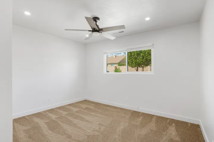 Recessed lighting, ceiling fan, white walls, carpet flooring, and a single window