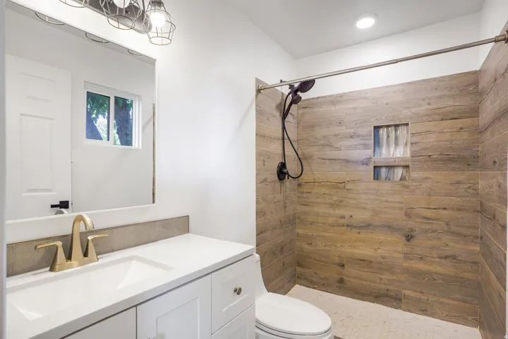 White vanity with a solid surface countertop, gold-finish faucet, and a rectangular undermount sink