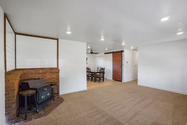 Brick fireplace with a wood-burning stove, recessed lighting, carpet flooring, a barn door, and wood-finish flooring in the adjoining area