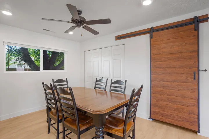 Recessed lighting, ceiling fan, wood-finish flooring, white double bi-fold doors, and a wood-finish barn door with black hardware