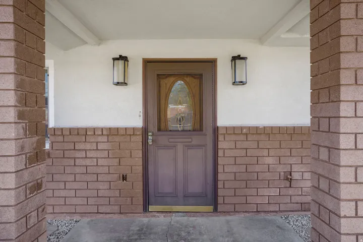 Brick facade with a contrasting white stucco finish, featuring two exterior sconces and a front entry door with an oval glass insert