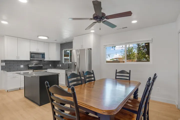 Kitchen featuring white cabinetry, stainless steel appliances, a dark tile backsplash, a center island with a stone-finish countertop, and wood-finish flooring