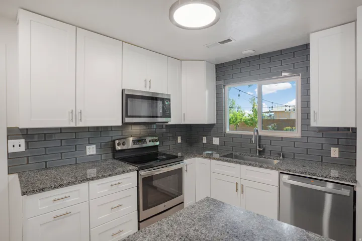 Kitchen featuring white shaker-style cabinetry, stainless steel appliances, speckled stone countertops, and a subway tile backsplash
