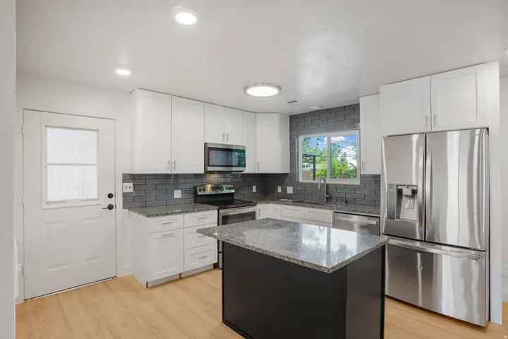 Kitchen featuring wood-finish flooring, white cabinetry, stainless steel appliances, a dark tile backsplash, and a central island with a contrasting base