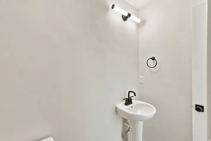 Pedestal sink with a matte black faucet, wall-mounted light fixture, and textured wall finish
