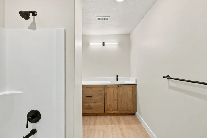 Shower stall with matte black fixtures, wood-finish vanity with a white countertop and integrated sink, and wood-finish flooring