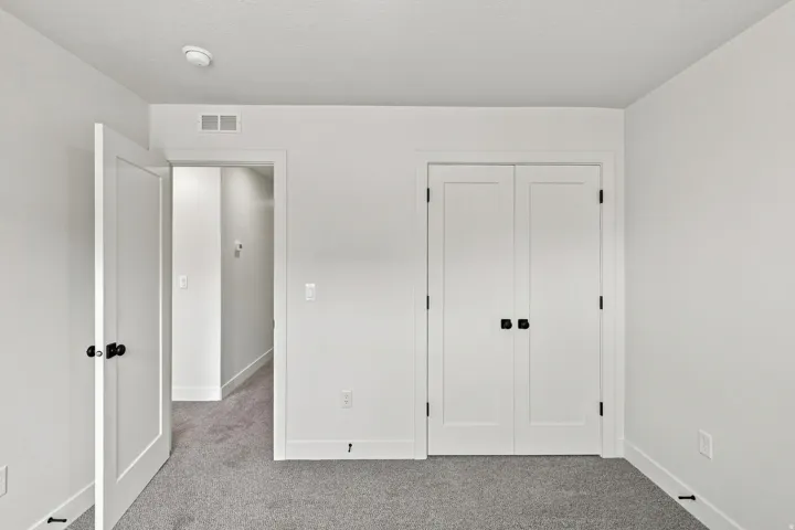 Light gray carpet flooring, white walls, white trim, white doors with black hardware, and an overhead lighting fixture